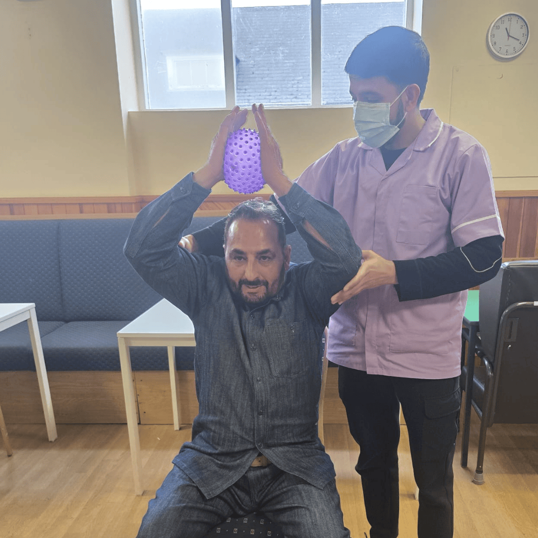Thumhara volunteer assisting asian gentleman with chair exercises